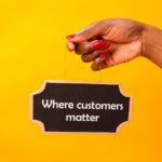 Hand holding a sign with 'Where customers matter' on a vibrant yellow backdrop.